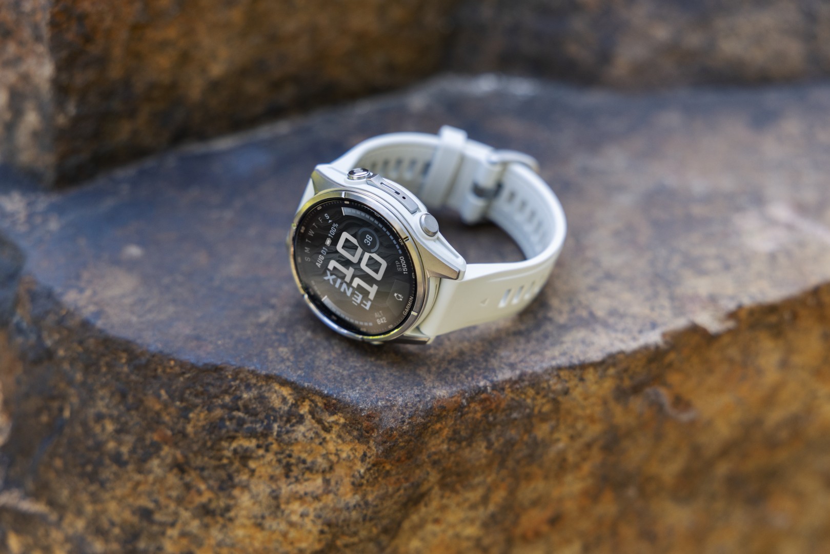 Montre Garmin Fenix 9 lunette titane et bracelet silicone gris cendré posée sur un rocher, altitude affichée au cadran