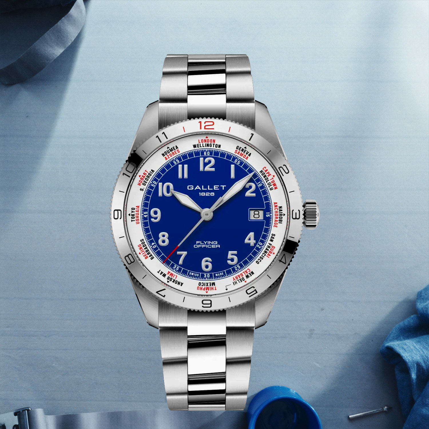 Montre Gallet Flying Officer Automatic 40 mm sur bracelet acier, posée sur un plan de travail clair à côté d'un mug émaillé et d'un tournevis d'horloger