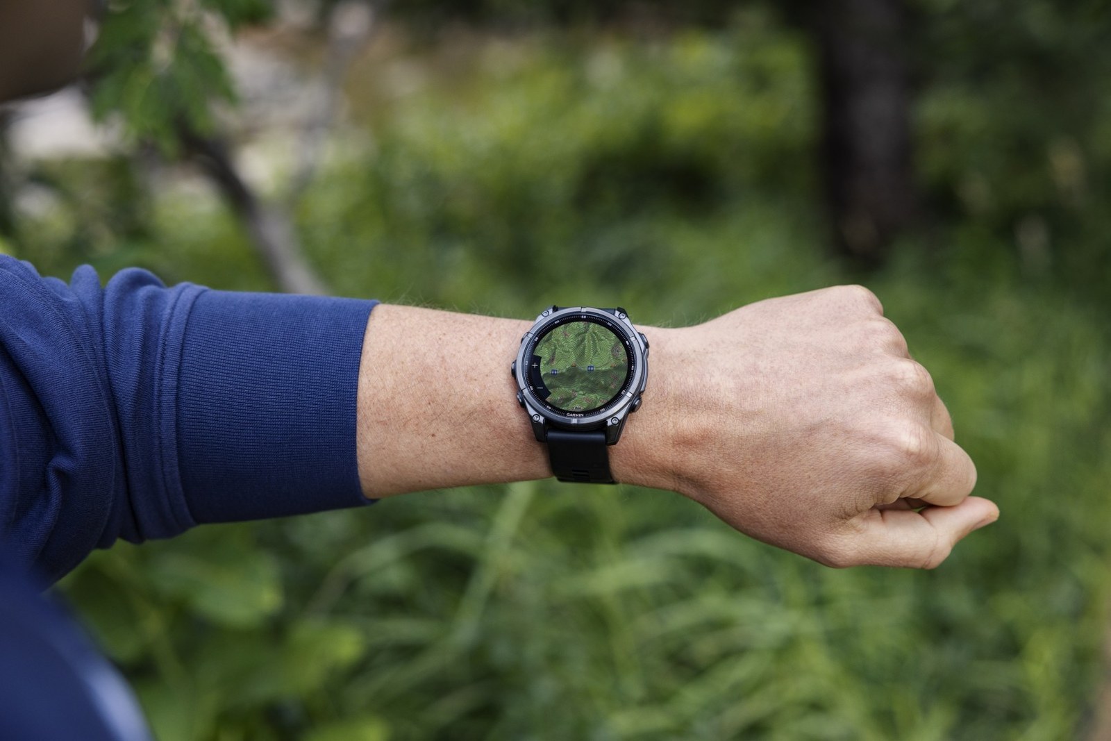Montre Garmin fēnix au poignet en forêt, carte topographique affichée à l'écran avec les boutons de zoom