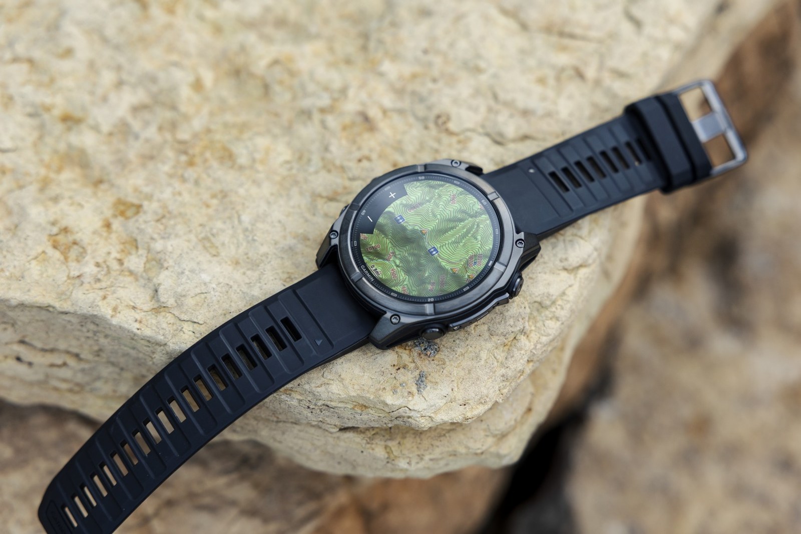 Montre Garmin fēnix posée sur un rocher, carte topographique et repères de parcours affichés à l'écran