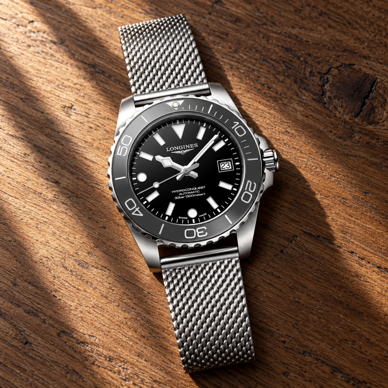 Longines HydroConquest 39 mm cadran noir laqué, lunette céramique grise et bracelet maille milanaise, sur des galets gris mouillés, vue d'illustration