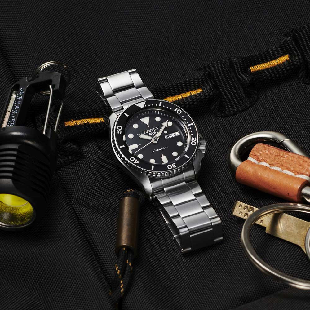 Montre Seiko 5 Sports SRPD55K1 automatique 42 mm, cadran noir, bracelet acier, à plat sur un comptoir d'ardoise vu de dessus, avec une loupe