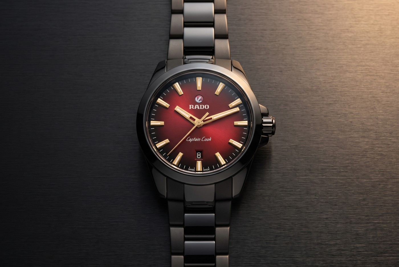 Rado Captain Cook Discover à cadran dégradé rouge et index ton or jaune, posée sur un métal noir brossé
